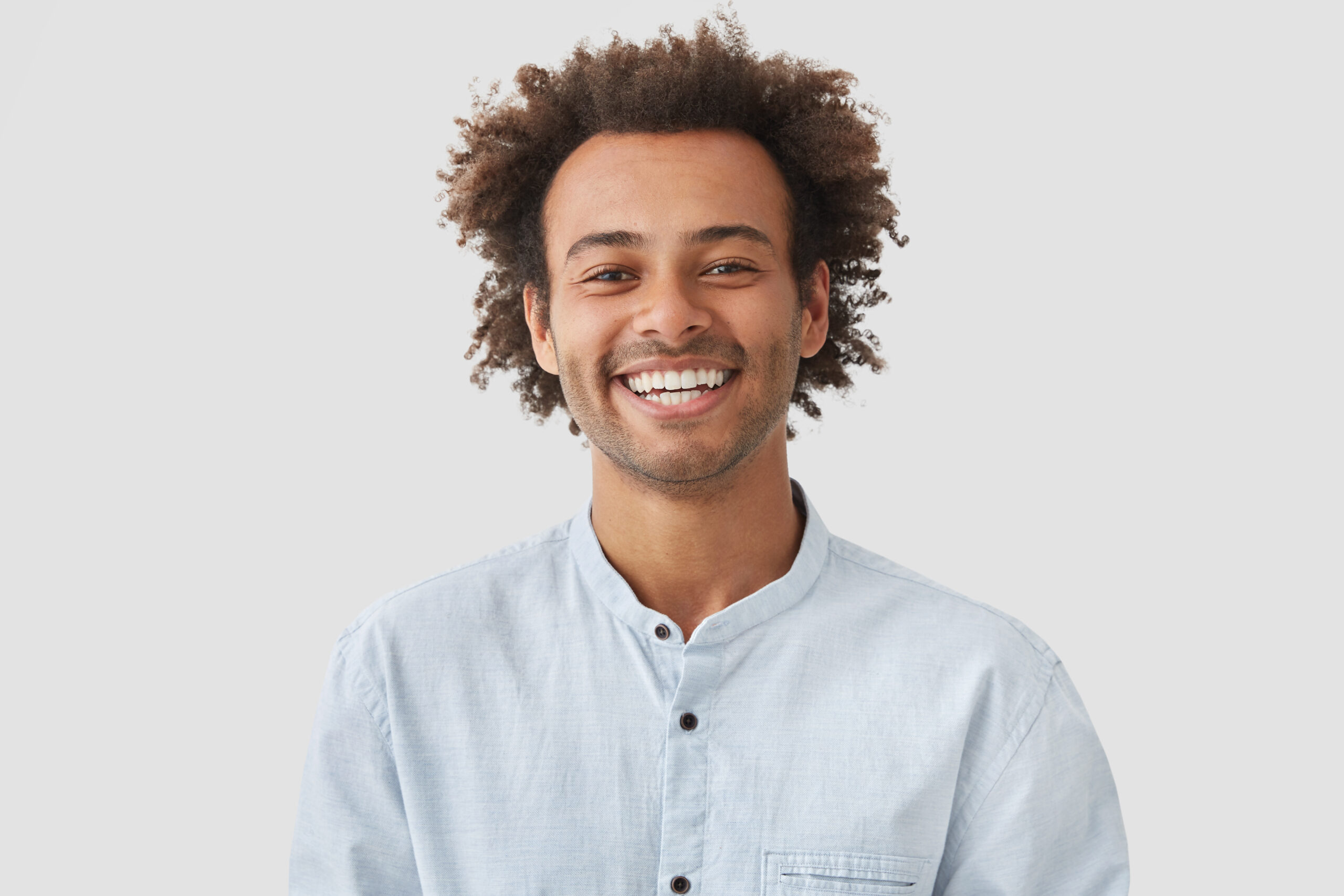 Happy mixed race male student with Afro hairdo shows white teeth, being in good mood after classes as going to have date with female groupmate, stands against white background. Positiveness concept